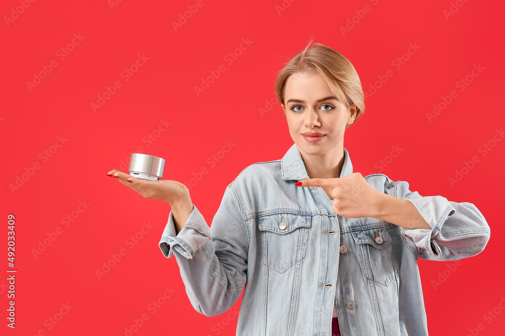 Young woman pointing at wireless portable speaker on red background