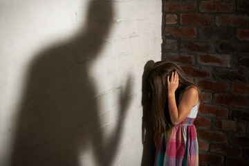 Defenceless victim. Abused little girl huddled over while the shadow of her abuser looms towards her.