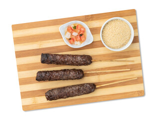 Wall Mural - Meat Kafta skewers over wooden board with farofa and vinaigrette isolated over white background