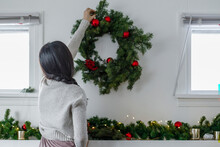 Young Woman Hanging Christmas Wreath Above Fireplace