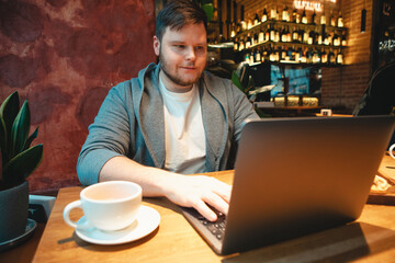 man freelancer working on laptop in cafe eating burger and drinking tea