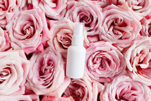 White Cosmetic Spray Bottle On Pink Roses Flower Texture Background. Mockup. Skincare Beauty And Liquid Antibacterial Spray. Natural Body Mist. Front View, Flat Lay. Bottle For Branding