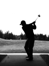 Silhouette Of A Man Mid Swing With His Driver As He Practices Golf At A Driving Range Facility During Off-season In Alberta Canada. Black And White