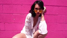 Beautiful Young Asian Woman In Squatting Position Posing To Camera By Pink Wall