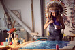 A young female artist with a war bonnet in the studio is mixing and preparing the paint for a new painting. Art, painting, studio