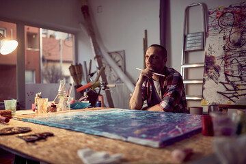 A young male artist is brainstorming while working on a new painting in the studio. Art, painting, studio