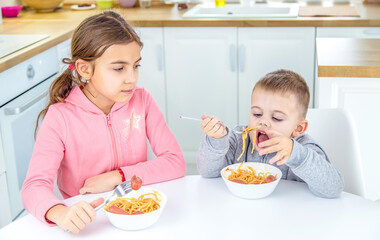 Wall Mural - children in the kitchen at the table eat pasta.