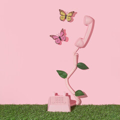 Spring creative layout with pink retro phone with butterflies and leaves on pastel pink background and green grass. 80s or 90s retro fashion aesthetic flowers concept. Minimal romantic idea.