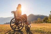 Disabled Handicapped Woman Is Sitting On Wheelchair At Sunset.