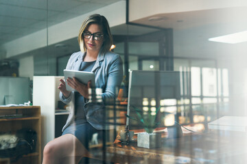 Poster - Technology keeps her one step ahead. Shot of a young businesswoman working late on a digital tablet in an office.
