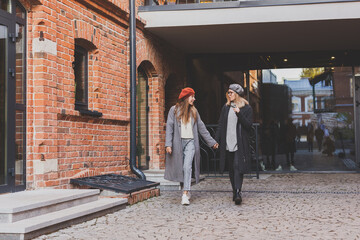 Two girls walking on street together and holding their hands. They are wearing spring or autumn clothes and they are happy. Friendship and relationship concept