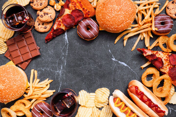 Wall Mural - Junk food frame over a dark background. Variety of take out and fast foods. Pizza, hamburgers, french fries, chips, hot dogs, sweets. Top view with copy space.