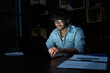 © insta_photos - Smiling young curly indian latin ethnic business man or student wearing glasses remote working overtime, learning online late at night at home or in dark office using laptop computer at workplace.