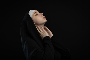 A nun on a black background raised her face to the sky. Postcard with a picture of a young girl with an empty space for your description