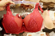 © Oleg - Woman choosing red bra in lingerie store. Female fashion, different sizes of lace underwear