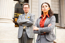 Serious Legal Or Business People On Steps With Arms Crossed Looking At Viewer. Focus Is On Woman's Face.