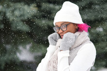 Portrait Of Happy Positive Girl, Black African Ethnic Afro American Young Woman Is Smiling Walking At Winter Cold Snowy Park In Snow At Cold Frosty Day In Warm Clothes Hat, Scarf Looking At Camera