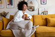© Daniel - Happy African american woman enjoying quiet time at home laughing, drinking morning coffee sitting on sofa. Copy space.
