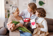 © JenkoAtaman - Happy International Mother's Day.Smiling  daughter and granddaughter giving flowers  and gift to grandmother   celebrate spring holiday Women's Day at home