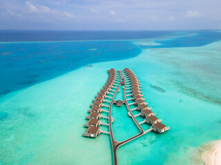 Wall Mural - Overwater villas and white sand beach on tropical island for holidays vacation travel and honeymoon. Luxury resort hotel in Maldives or Caribbean with turquoise sea water. Drone aerial view.