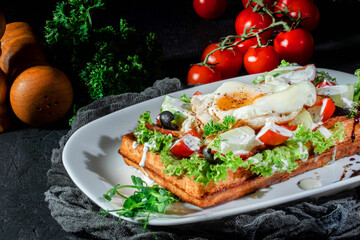 Wall Mural - Waffle with fried egg and vegetables on dark background. Delicious traditional breakfast idea. Viennese waffles, belgian waffle recipe