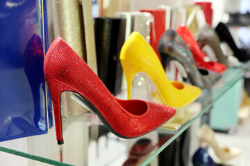 Shoes on high heels and handbags on glass rack in a store. Different colors of spring and summer female footwear