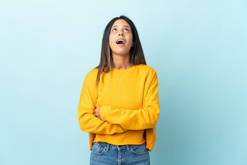 Poster - Caucasian girl isolated on blue background looking up and with surprised expression