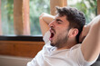 © Tof - Photographie - jeune homme assis dans un fauteuil qui s'étire en baillant. Il se repose car il est fatigué. On voit le jardin en arrière plan