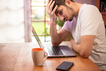 gros plan sur le visage d'un jeune homme fatigué en train de travailler devant son ordinateur dans son bureau. il se tient la tête, il a des problèmes