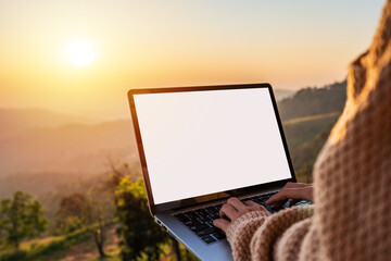 Wall Mural - Young woman freelancer traveler working online using laptop and enjoying the beautiful nature landscape with mountain view at sunrise