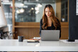 © David - Charming Asian businesswoman sitting in the office with a digital laptop computer. Excited Asian businesswoman raising hands to congratulate while working in a modern office,