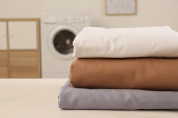 Poster - Stack of clean bed linens on white wooden table in laundry room