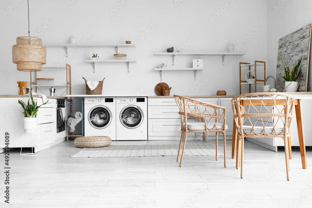 Interior of light kitchen with washing machines, white counters and dining table