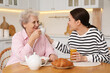 © New Africa - Young caregiver and senior woman having breakfast at table in kitchen. Home care service