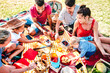 Multiracial families having fun together with kids at park on pic nic party - Genuine joy and love life style concept with mixed age people toasting juices with children at park - Warm bright filter