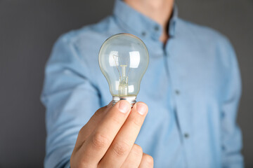 Wall Mural - Man holding incandescent light bulb on grey background, closeup