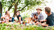 Friends Group Having Fun Moment At Pic Nic Playing Guitar On Sunset - Friendship Life Style Concept With Young People Enjoying Springtime Camping Together At Park Location - Bright Greenish Filter