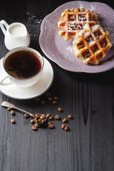 Wall Mural - Homemade belgian waffles, white ceramic cup of coffee, milk, teaspoon and coffee beans. Dark rustic background. Space for text in the center.