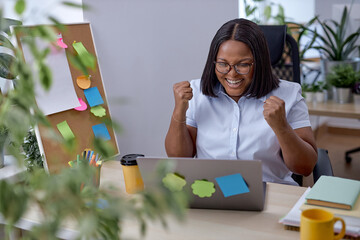 Wall Mural - excited black American woman in formal wear looking at laptop screen, excited by good news, reading email, online lottery win or money refund, job promotion,received great exam results, raising fists