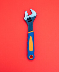 Poster - Adjustable wrench with graduated scale, orange, blue color rubber handle on red background. Vertical