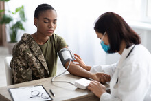 Black Soldier Lady Sitting At Table While Doctor Checking Her Blood Pressure