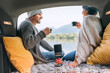 © Soloviova Liudmyla - Car trunk view of chatting couple dressed warm knitted clothes enjoying gas stove prepared coffee and mountain lake view. Cozy early autumn couple auto traveling concept image..