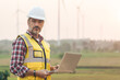 © ztony1971 - Portrait of power engineer wearing safety jacket and hardhat with laptop computer working at outdoor field site that have wind turbine at the background.
