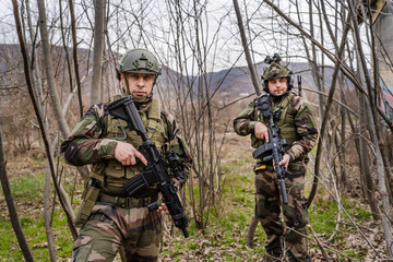 Two men front view portrait of soldiers in camouflage uniform armed with rifle ready to go on a mission in war zone stand outdoor in nature looking to the camera dogs of war mercenaries or volunteers