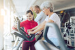 © Kzenon - Fitness coach in gym helping senior people during cardio bike training
