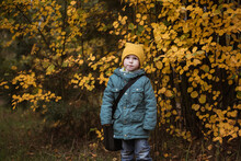 Little Caucasian Boy In Green Coat Against Yellow Bush Autumn Time