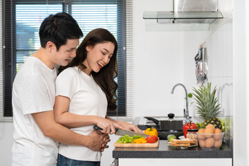 Wall Mural - couple cutting vegetables for preparing healthy food in the kitchen at home. man is hugging woman