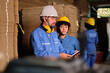 © tigercat_lpg - Asian male engineer in safety uniform and hard hat and female worker colleague inspect storage, stock order at factory warehouse, piles of stacking cardboard manufacture, industry product management.