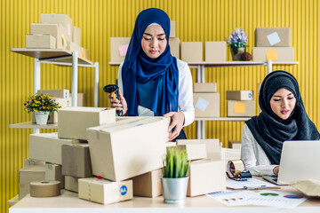 Wall Mural - Muslim two asian woman freelancer sme business online shopping working and checklist order with cardboard box on table at home - Business online shipping and delivery concept