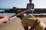 Fototapeta  - Young man bending backwards and passing under ribbon when ing limbo game with friends on beach
